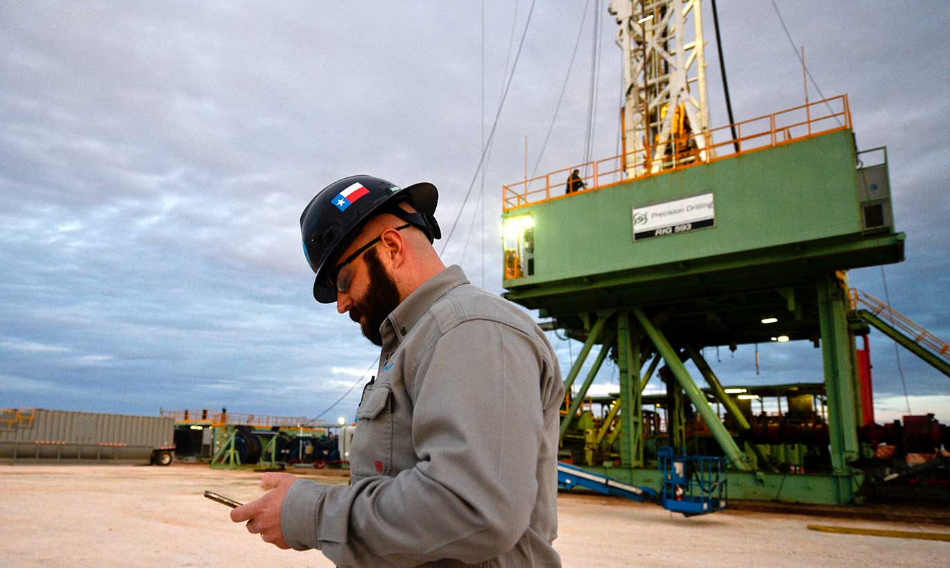 Oil and gas worker in Midland, Texas checks his phone while walking around the perimeter of the rig