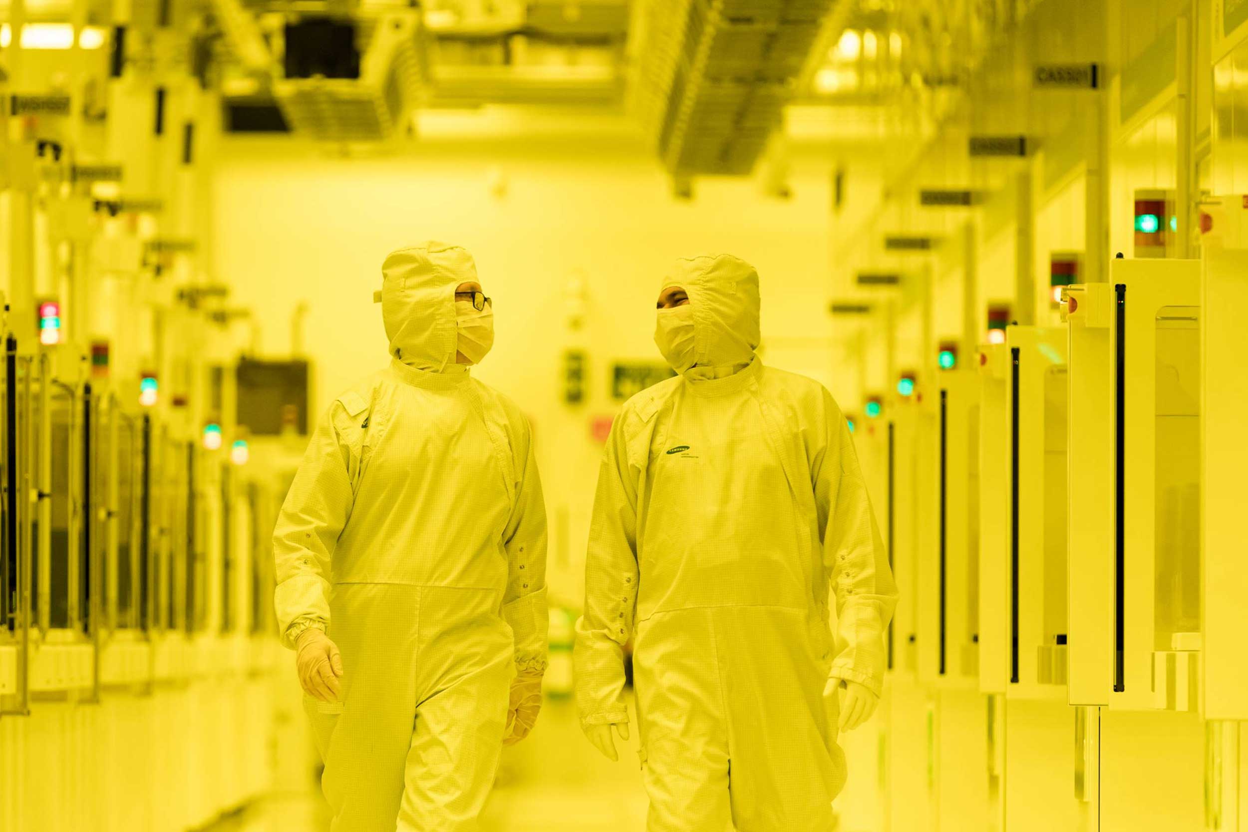 Two people walk down a hallway in hazmat suits