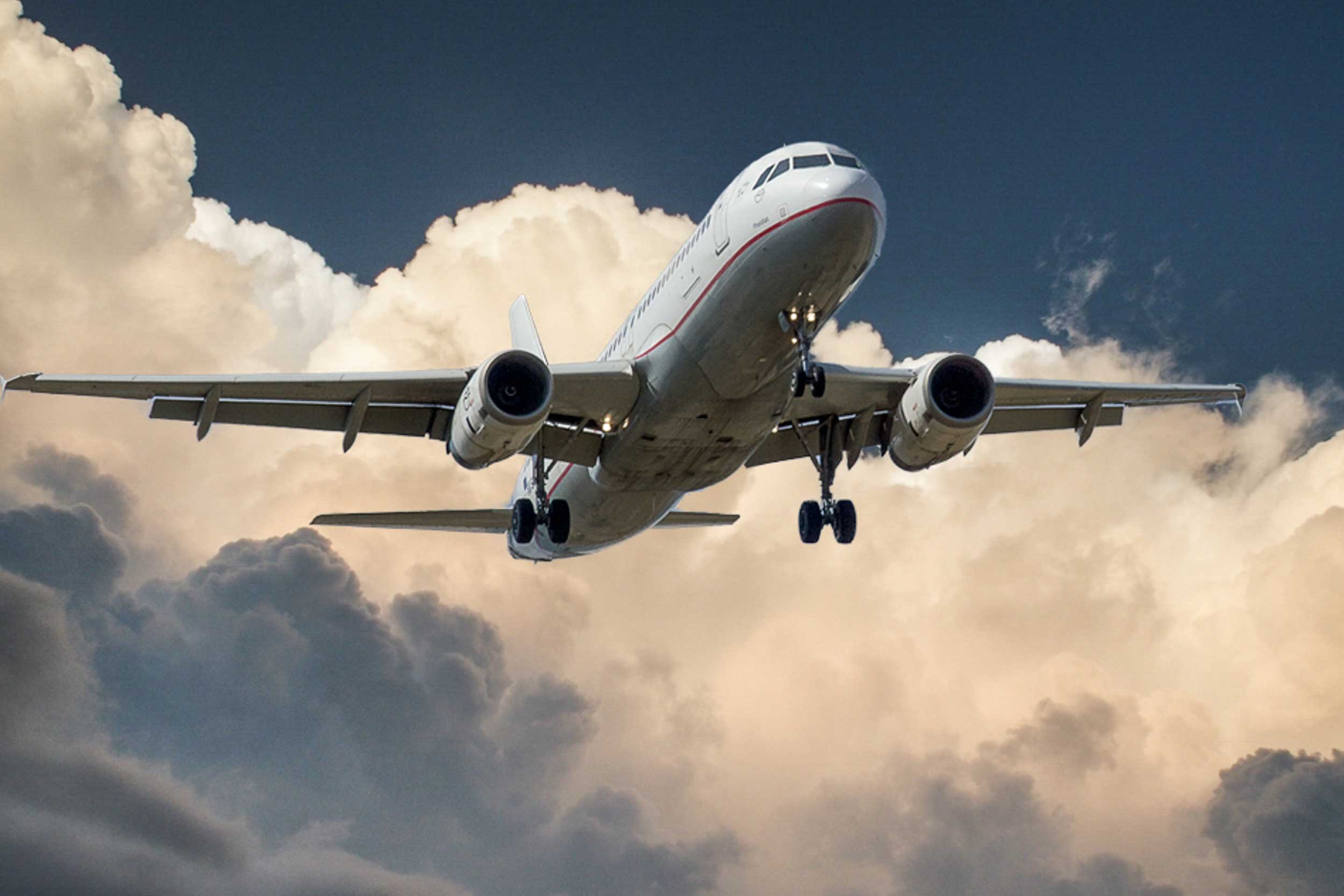 A large commercial airplane flies in front of white clouds.