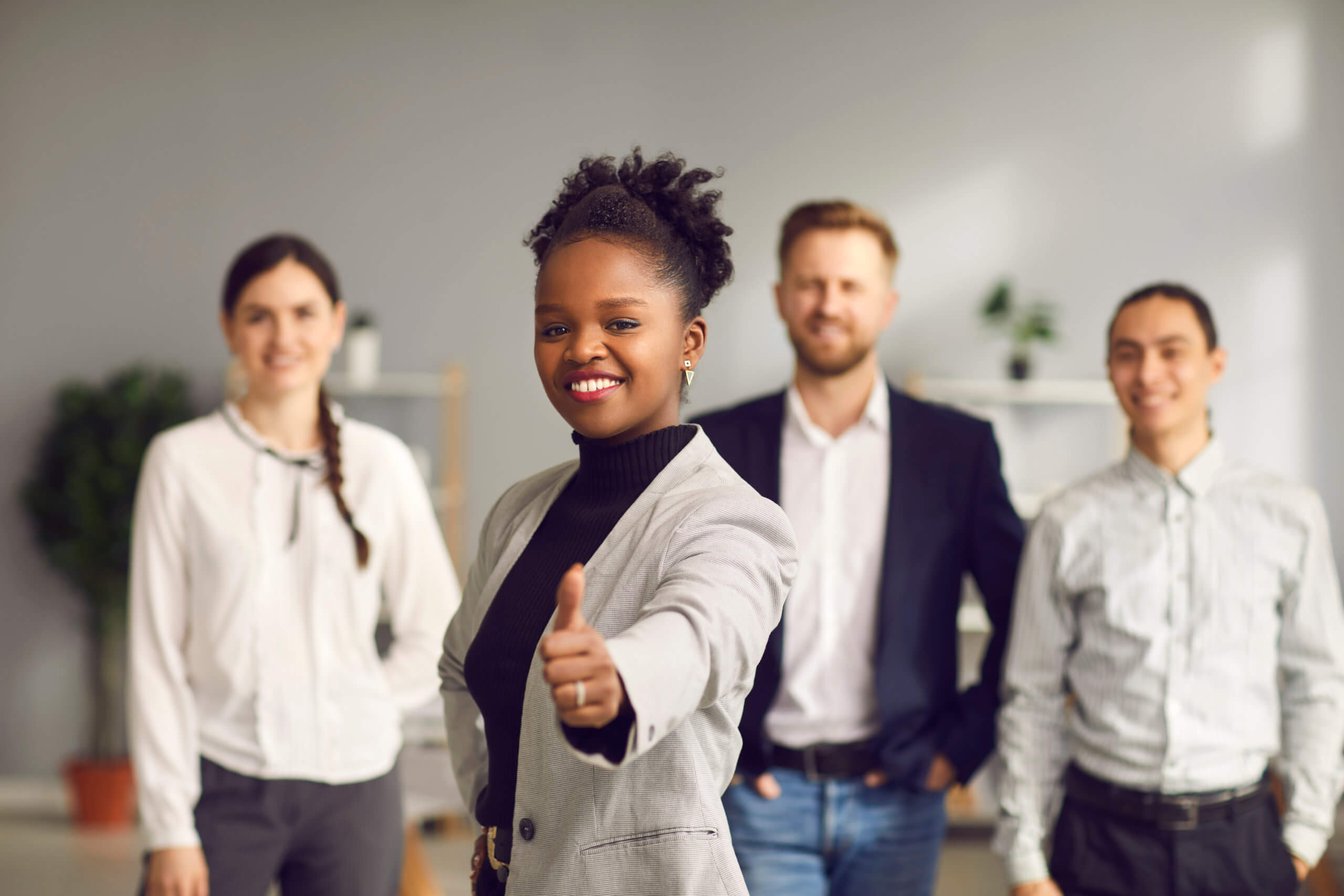 Smiling young woman giving thumbs-up together with diverse multiracial people in background