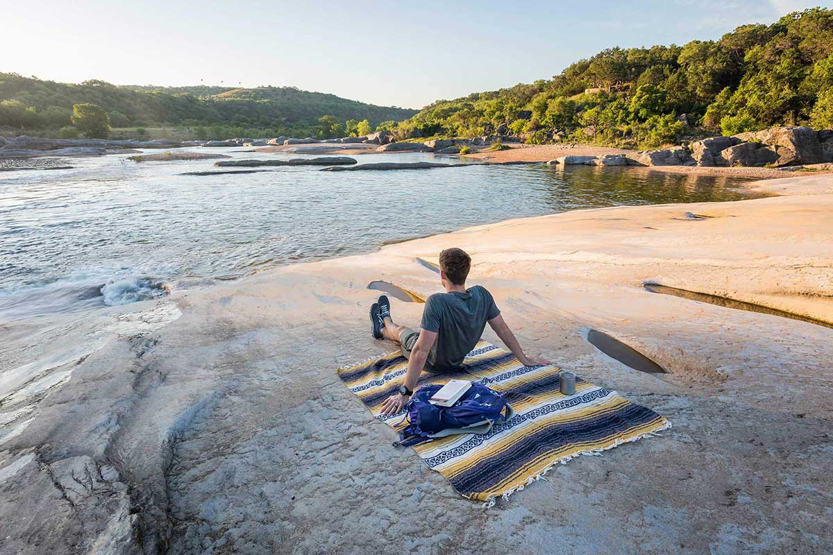 Man looking out at a Texas lake while sitting on a blanket on a rock face shore